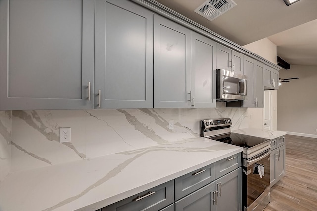 kitchen with appliances with stainless steel finishes, gray cabinets, and backsplash