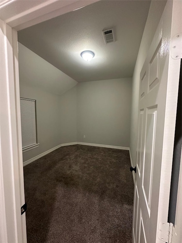 carpeted empty room featuring vaulted ceiling and a textured ceiling