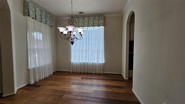 unfurnished dining area with a textured ceiling, a chandelier, dark wood-type flooring, visible vents, and crown molding