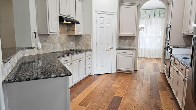 kitchen featuring light wood-style flooring, under cabinet range hood, black electric cooktop, white cabinets, and dark stone counters