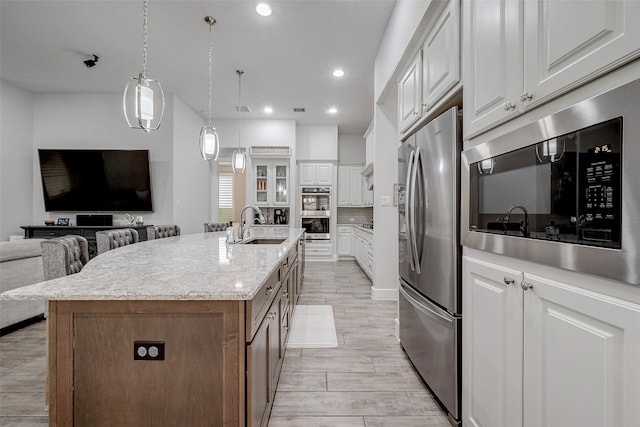 kitchen with sink, appliances with stainless steel finishes, a kitchen island with sink, backsplash, and white cabinets