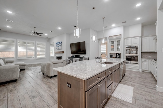 kitchen featuring sink, appliances with stainless steel finishes, white cabinetry, a center island with sink, and decorative light fixtures