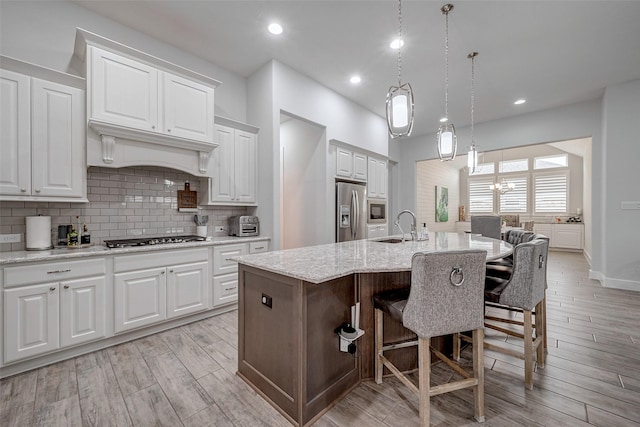 kitchen featuring a breakfast bar area, white cabinets, a kitchen island with sink, light stone counters, and stainless steel appliances