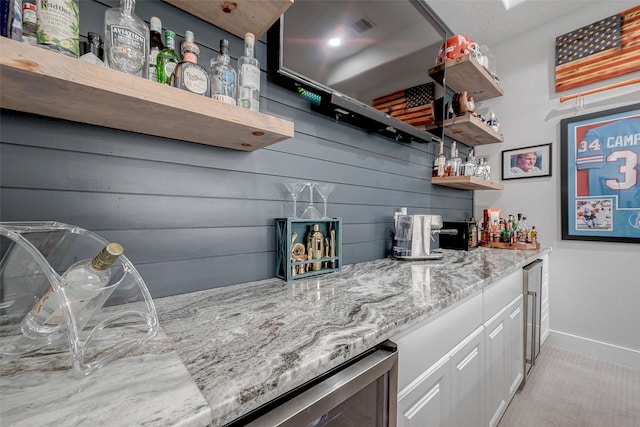 bar featuring light stone counters and white cabinets