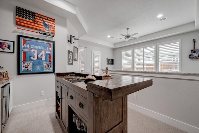 kitchen featuring ceiling fan, a kitchen island, a raised ceiling, and light carpet