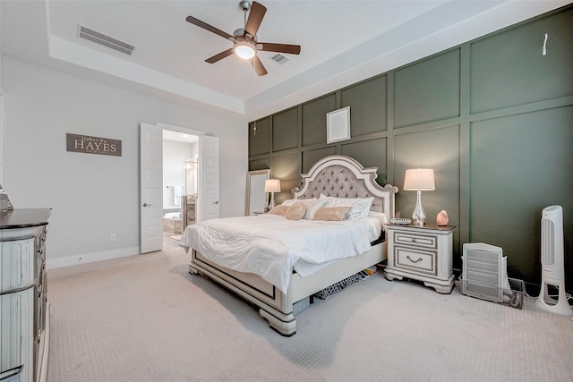 carpeted bedroom featuring a raised ceiling, ensuite bathroom, and ceiling fan