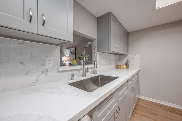 kitchen featuring sink, gray cabinets, light stone counters, light hardwood / wood-style floors, and decorative backsplash