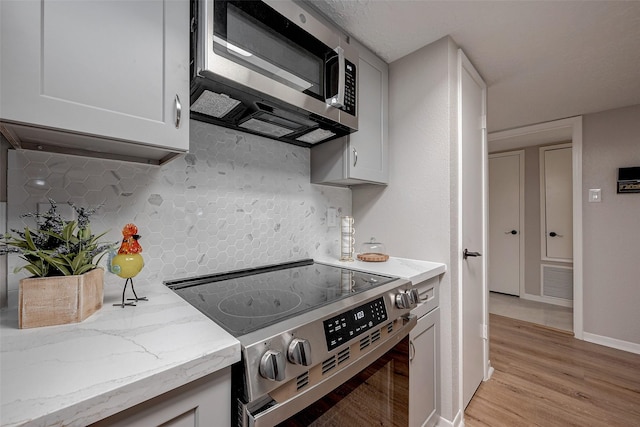 kitchen featuring backsplash, light hardwood / wood-style flooring, white cabinets, and appliances with stainless steel finishes