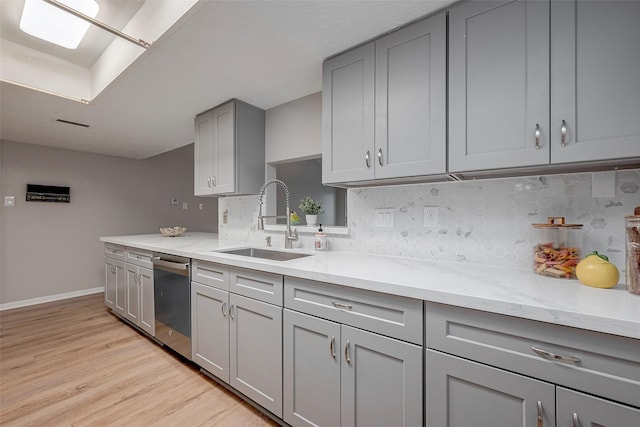 kitchen featuring sink, dishwasher, gray cabinetry, tasteful backsplash, and light wood-type flooring