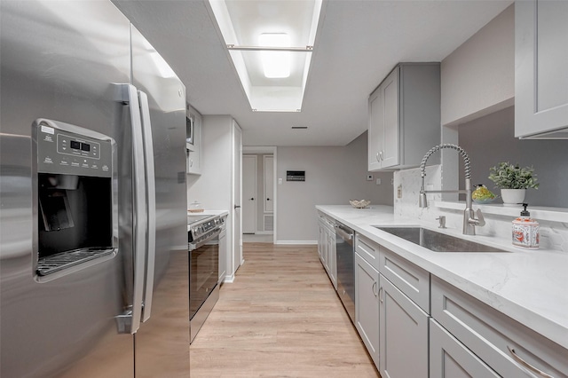 kitchen featuring stainless steel appliances, light stone countertops, sink, and light hardwood / wood-style flooring