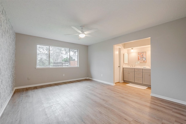 unfurnished bedroom featuring ceiling fan, ensuite bath, sink, and light wood-type flooring