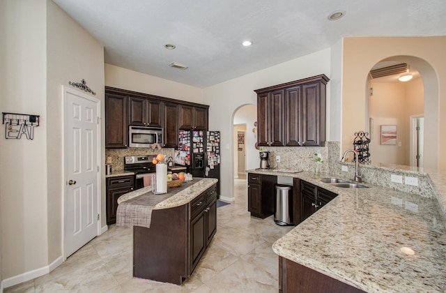 kitchen with light stone countertops, appliances with stainless steel finishes, sink, and dark brown cabinets