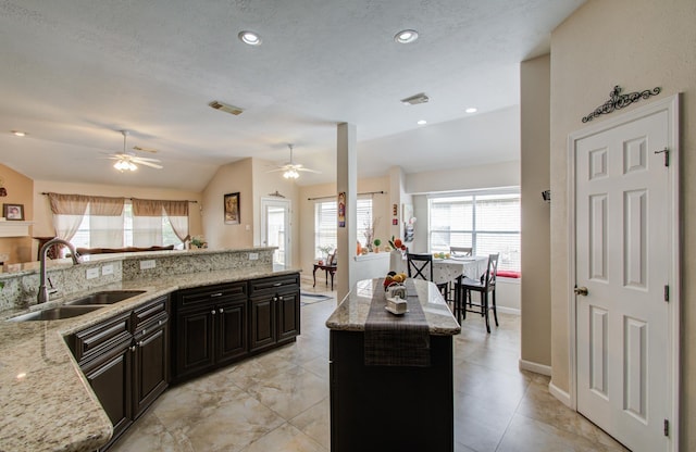 kitchen featuring light stone counters, sink, lofted ceiling, and a kitchen island