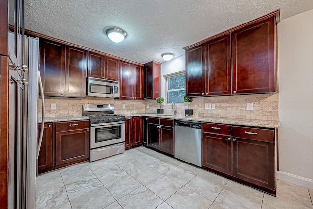 kitchen with sink, light tile patterned floors, backsplash, stainless steel appliances, and light stone countertops