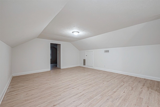 bonus room featuring lofted ceiling, a textured ceiling, and light hardwood / wood-style flooring