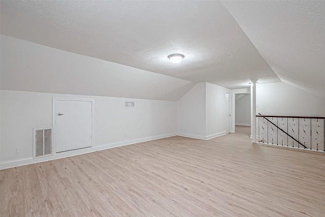 bonus room featuring vaulted ceiling, light wood-type flooring, and a textured ceiling