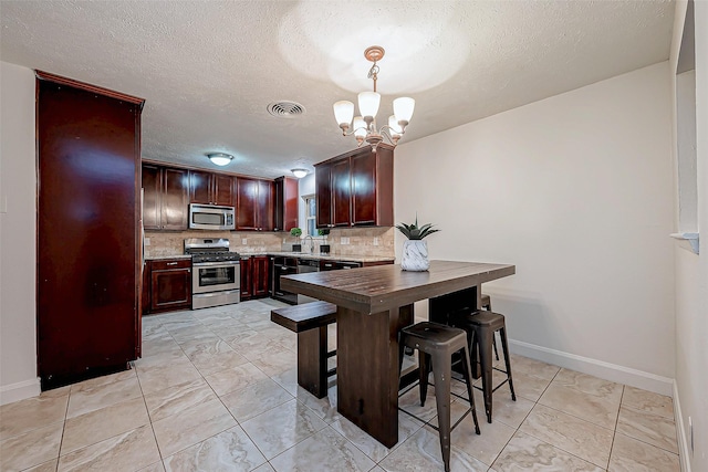 kitchen with appliances with stainless steel finishes, pendant lighting, sink, decorative backsplash, and an inviting chandelier