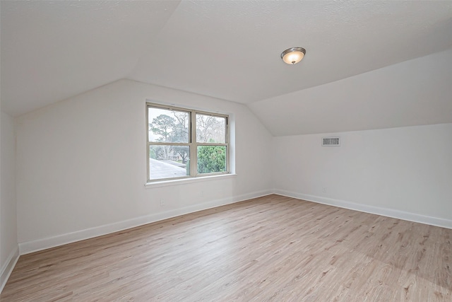 additional living space with lofted ceiling, a textured ceiling, and light wood-type flooring