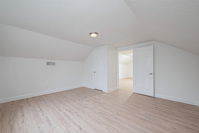 bonus room featuring lofted ceiling, light hardwood / wood-style floors, and a textured ceiling