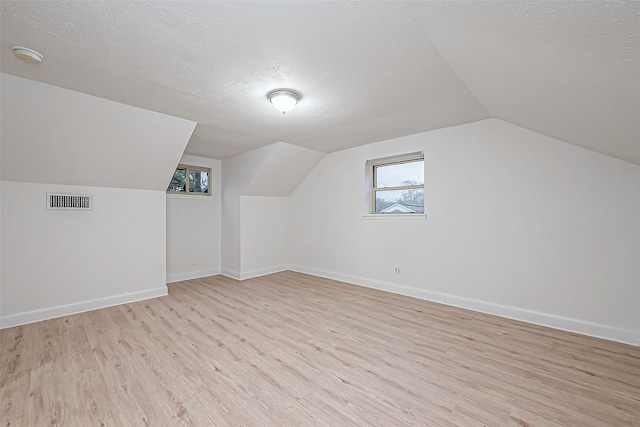 bonus room featuring vaulted ceiling, a textured ceiling, and light hardwood / wood-style flooring