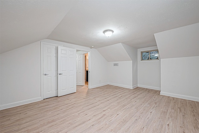 bonus room featuring vaulted ceiling, a textured ceiling, and light wood-type flooring