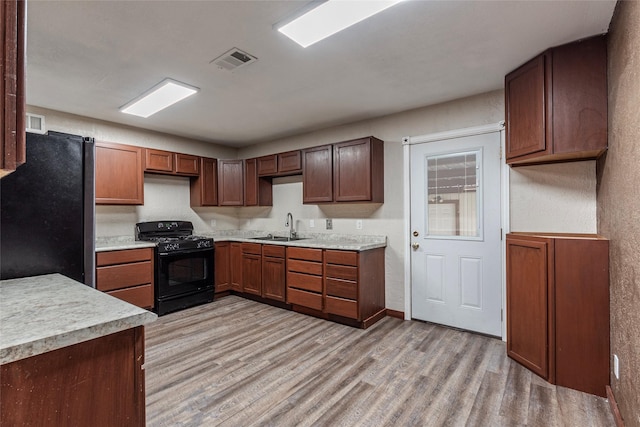 kitchen with visible vents, a sink, freestanding refrigerator, light wood finished floors, and black range with gas cooktop