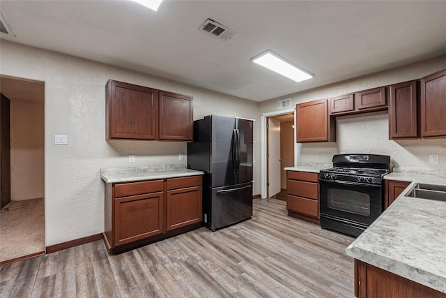 kitchen with freestanding refrigerator, light wood-style floors, visible vents, and black range with gas stovetop