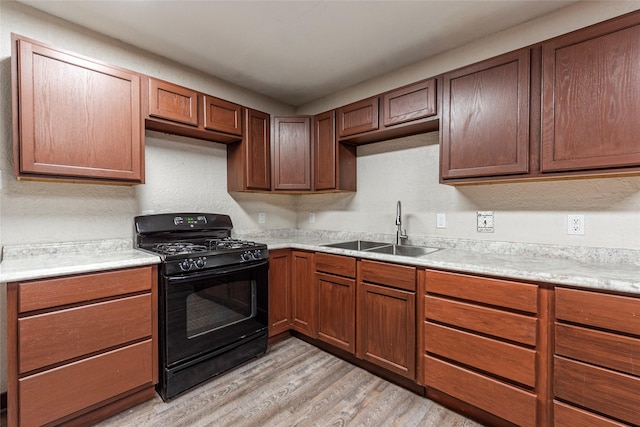 kitchen with black gas stove, light countertops, light wood-style flooring, a textured wall, and a sink