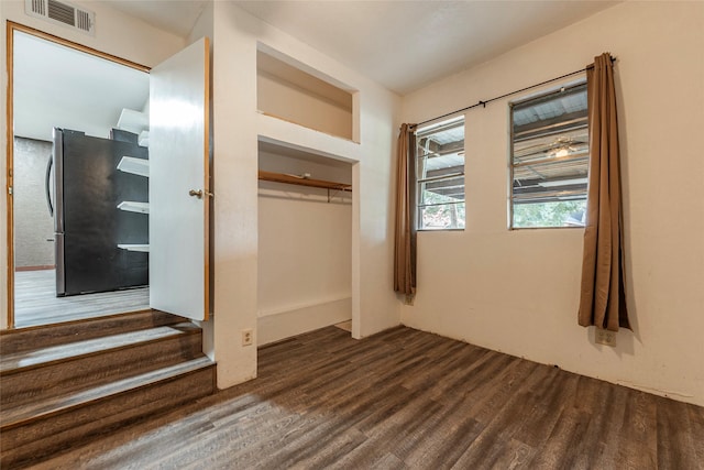 unfurnished bedroom with dark wood finished floors, visible vents, freestanding refrigerator, and a closet