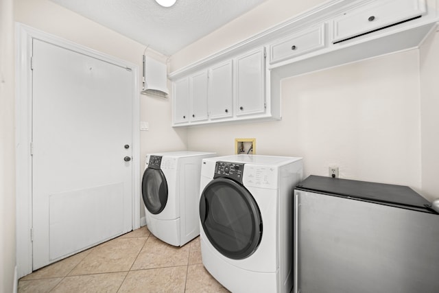 clothes washing area featuring cabinet space, light tile patterned floors, washer and clothes dryer, and a textured ceiling