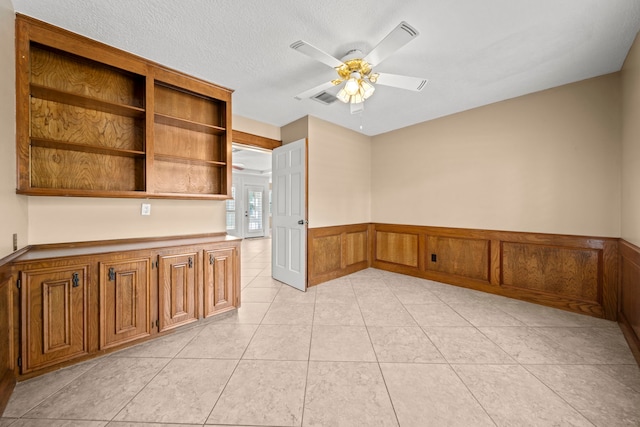 empty room with wainscoting, ceiling fan, a textured ceiling, and light tile patterned flooring