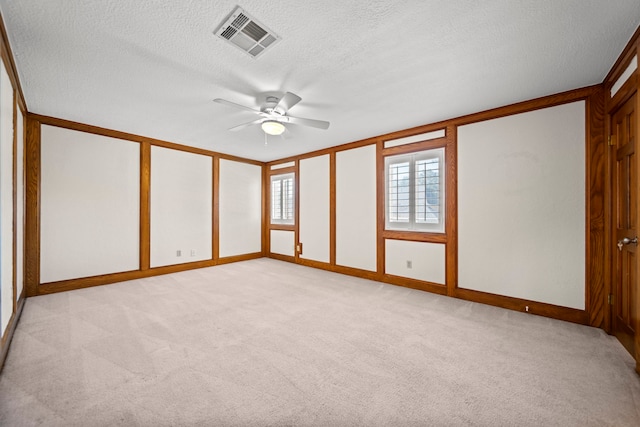 empty room featuring light carpet, ceiling fan, visible vents, and a textured ceiling