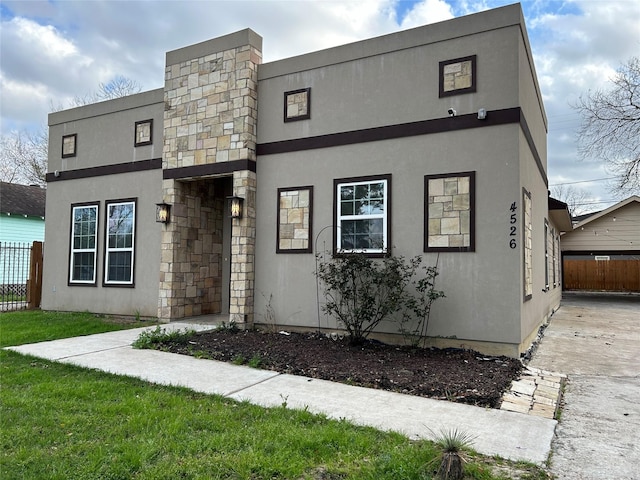 view of front facade featuring fence, stone siding, and stucco siding