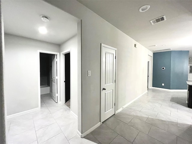 hallway with light tile patterned floors, visible vents, and baseboards