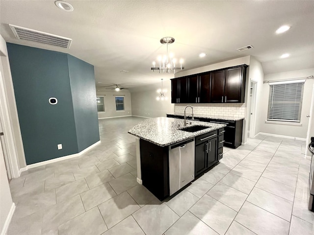 kitchen featuring light stone counters, stainless steel dishwasher, pendant lighting, sink, and a kitchen island with sink