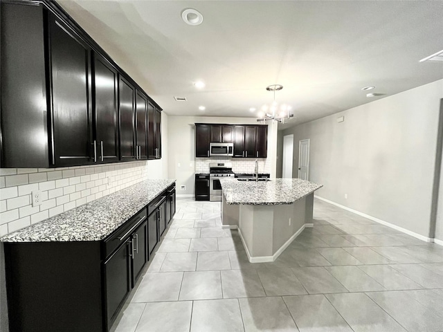 kitchen with backsplash, light stone countertops, appliances with stainless steel finishes, an inviting chandelier, and a sink