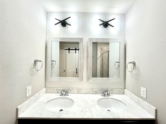 bathroom featuring double vanity, a textured wall, a stall shower, and a sink