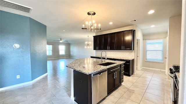 kitchen featuring sink, stainless steel appliances, an island with sink, light stone countertops, and decorative backsplash