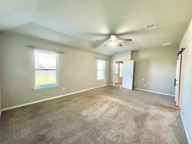 unfurnished bedroom featuring vaulted ceiling, ceiling fan, a barn door, and carpet floors