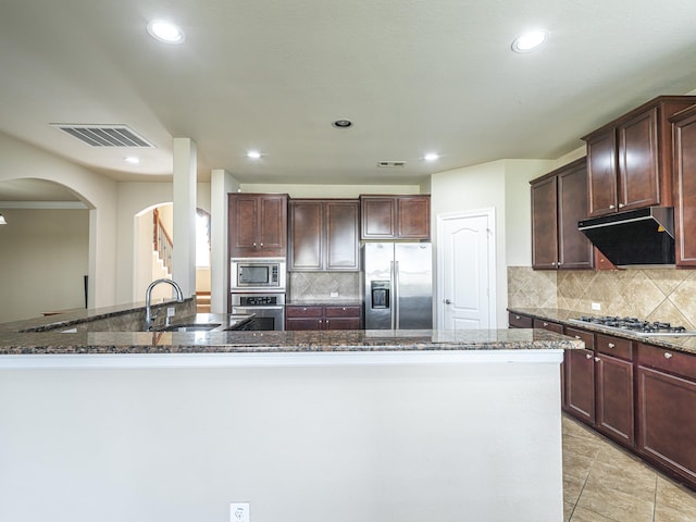 kitchen featuring sink, dark stone countertops, backsplash, dark brown cabinets, and stainless steel appliances