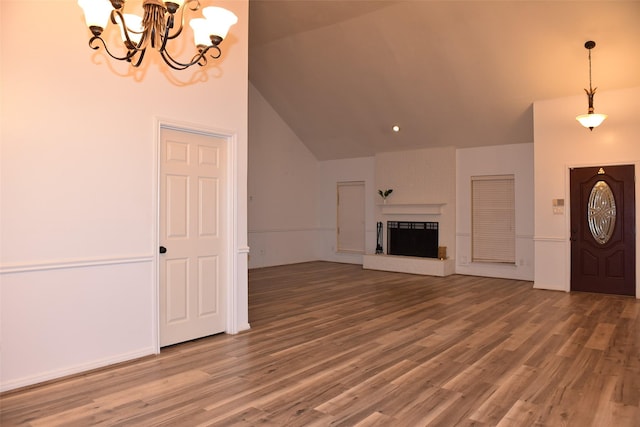 unfurnished living room featuring an inviting chandelier, a fireplace, wood-type flooring, and vaulted ceiling