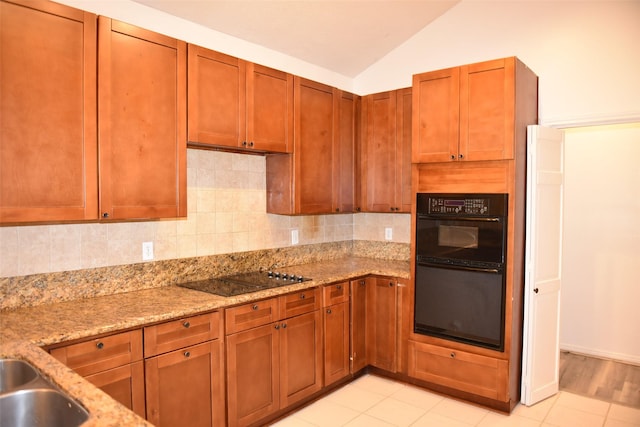 kitchen with lofted ceiling, light stone counters, black appliances, light tile patterned floors, and backsplash