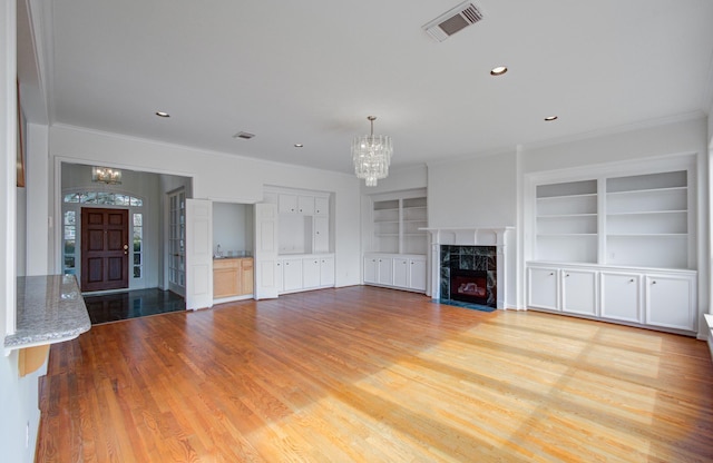 unfurnished living room with ornamental molding, light wood-type flooring, a fireplace, and an inviting chandelier