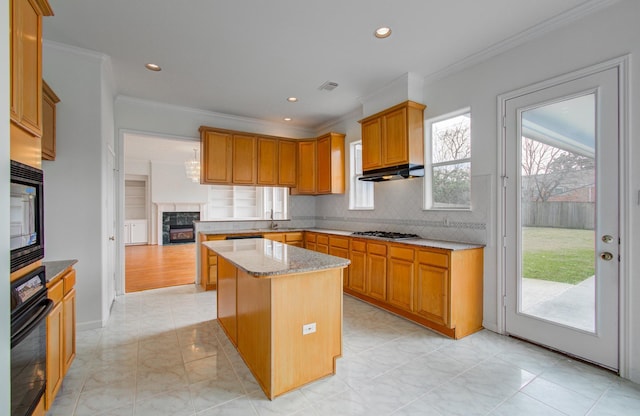 kitchen featuring backsplash, a center island, black appliances, light stone countertops, and a tiled fireplace