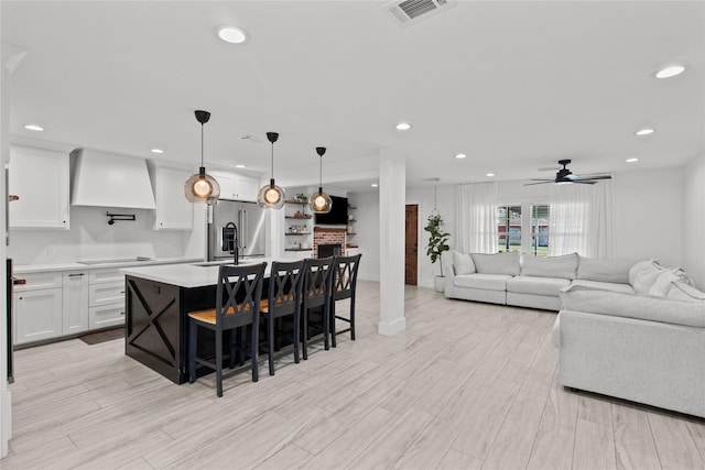 kitchen featuring high end fridge, white cabinetry, a center island with sink, pendant lighting, and wall chimney range hood