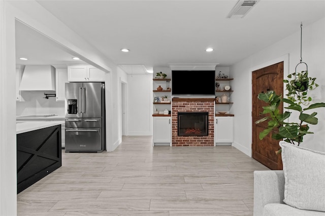 kitchen featuring high end fridge, a brick fireplace, custom range hood, and white cabinets