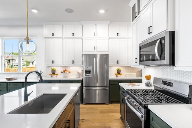 kitchen with stainless steel appliances, white cabinetry, hanging light fixtures, and sink