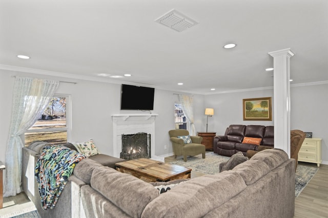 living room featuring a fireplace, light wood-type flooring, ornamental molding, and ornate columns