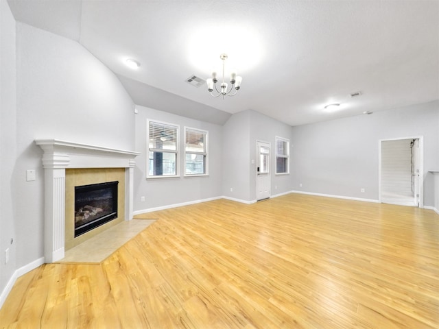 unfurnished living room featuring an inviting chandelier, a fireplace, vaulted ceiling, and light wood-type flooring