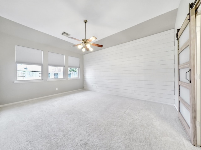 empty room with ceiling fan, light colored carpet, a barn door, and wood walls